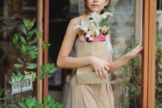 A woman carrying a paper bag with a beautiful bouquet exits a flower shop.